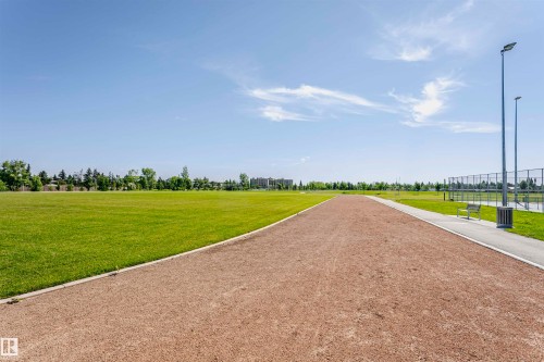 Expansive outdoor recreational area featuring a red cinder track, manicured green space, paved pathways, contemporary light poles, and perimeter fencing - 11440 44A Avenue, Edmonton, AB 