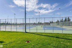Multiple hard-surface tennis courts featuring light blue playing areas and lime green surrounds, enclosed by chain-link fencing - 
