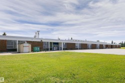 Single-story brick structure with multiple large windows, a flat white roofline, and a paved parking area - 