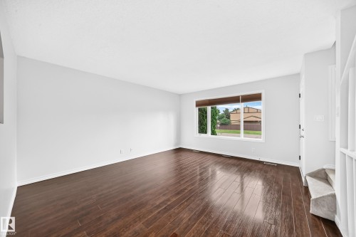 Spacious room with dark wood-finish flooring, white walls, and a large multi-pane window - 11447 22 Avenue Nw, Edmonton, AB 