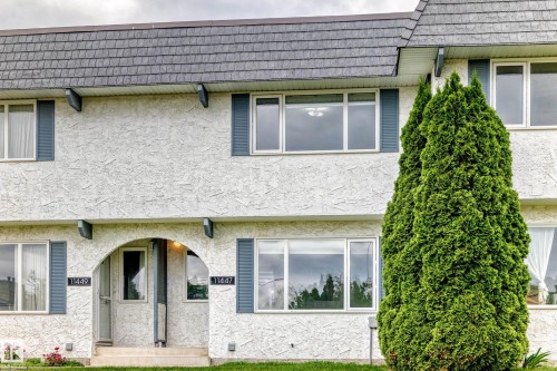 Multi-story exterior with textured stucco finish, dark gray shingle roofing, and blue decorative shutters - 11447 22 Avenue Nw, Edmonton, AB 