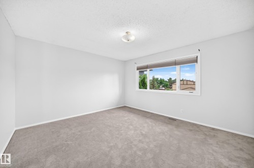 Spacious interior room featuring light gray carpeting, white walls, and a large window with white trim - 11447 22 Avenue Nw, Edmonton, AB 