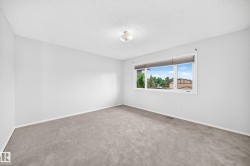 Spacious interior room featuring light gray carpeting, white walls, and a large window with white trim - 