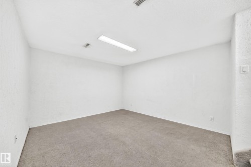 Spacious room featuring neutral carpeting, white painted walls, and a white ceiling with recessed lighting - 11447 22 Avenue Nw, Edmonton, AB 