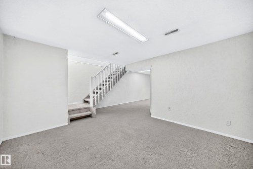 Carpeted room featuring a staircase with white railing, recessed lighting, and white baseboards - 11447 22 Avenue Nw, Edmonton, AB 