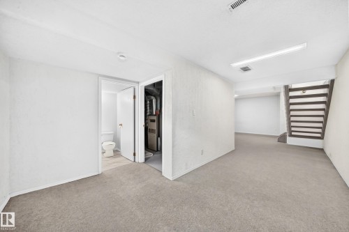 Carpeted lower level featuring a light neutral color palette, recessed lighting, and a partially visible bathroom with a toilet - 11447 22 Avenue Nw, Edmonton, AB 