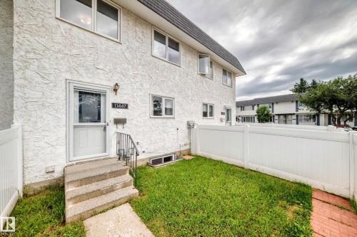 Stucco exterior with multiple windows, a concrete staircase, and a white screen door - 11447 22 Avenue Nw, Edmonton, AB 