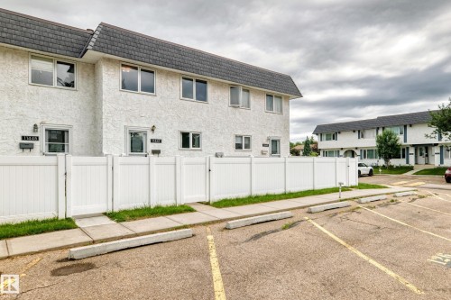 Multi-unit residential building featuring a textured white exterior, contrasting dark shingle roof, and white-framed windows - 11447 22 Avenue Nw, Edmonton, AB 