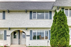 Stucco exterior featuring an arched entryway, shingle roof, and multiple windows with dark shutters - 