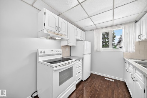 Kitchen featuring white cabinetry, dark wood-finish flooring, and white appliances - 11447 22 Avenue Nw, Edmonton, AB 
