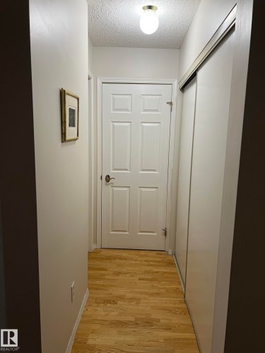 Hallway featuring wood-finish flooring, a six-panel door, and a sliding closet door with a metal track - 207 18012 95 Avenue, Edmonton, AB - Indoor Photo Showing Other Room