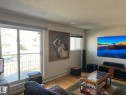 Living area featuring wood-finish flooring, white walls, and a sliding glass door opening to a balcony with a white metal railing - 207 18012 95 Avenue, Edmonton, AB  - Indoor Photo Showing Living Room 