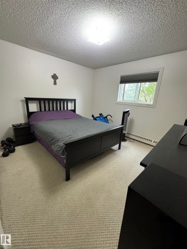 Bedroom featuring a textured ceiling, a flush-mount ceiling light, white walls, and light-toned carpet flooring - 207 18012 95 Avenue, Edmonton, AB 