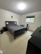 Bedroom featuring a textured ceiling, a flush-mount ceiling light, white walls, and light-toned carpet flooring - 