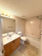 Bathroom featuring a vanity with wood-finish cabinetry and an integrated sink, a full-width mirror, a toilet, and a bathtub with tile surround - 