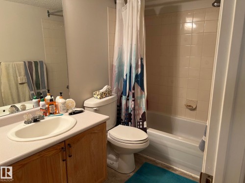 Bathroom featuring a vanity with a laminate countertop, integrated sink, and wood-finish cabinetry - 207 18012 95 Avenue, Edmonton, AB - Indoor Photo Showing Bathroom