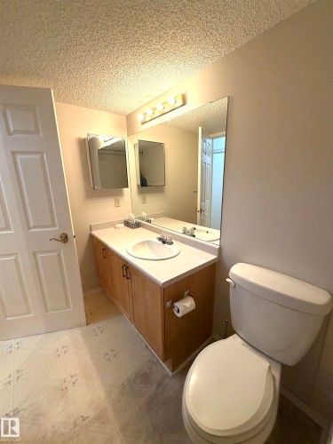 Bathroom featuring a single vanity with wood-finish cabinetry, a white countertop, and an integrated sink with a chrome faucet - 207 18012 95 Avenue, Edmonton, AB 