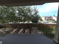 Balcony featuring a textured flooring surface and metal railings, overlooking mature trees, fenced grounds, and residential street - 