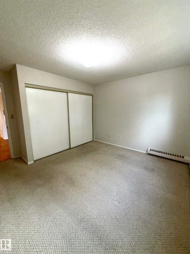 Carpeted room featuring a ceiling-mounted light fixture, white walls, and a baseboard heater - 207 18012 95 Avenue, Edmonton, AB 