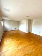 Spacious room featuring wood flooring, white walls, and a window for natural light - 
