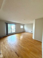 Spacious room featuring wood-finish flooring, light-toned walls, and a large sliding glass door with blinds - 