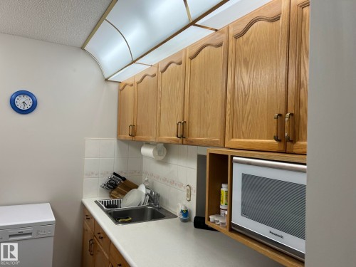 Kitchenette featuring wood-finish cabinetry, built-in microwave, white tile backsplash, a single basin sink, and an integrated overhead light fixture - 207 18012 95 Avenue, Edmonton, AB - Indoor Photo Showing Kitchen With Double Sink