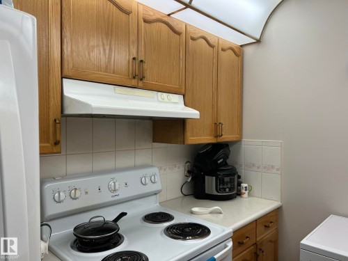 Kitchen area with wood-finish cabinetry and a white range hood - 207 18012 95 Avenue, Edmonton, AB - Indoor Photo Showing Kitchen