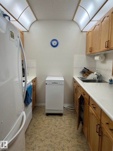 Galley kitchen featuring light wood cabinetry, white countertops, a white refrigerator, and a stainless steel sink - 207 18012 95 Avenue, Edmonton, AB - Indoor Photo Showing Laundry Room