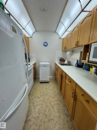 Galley kitchen featuring wood cabinetry, white laminate countertops, and a white tile backsplash - 