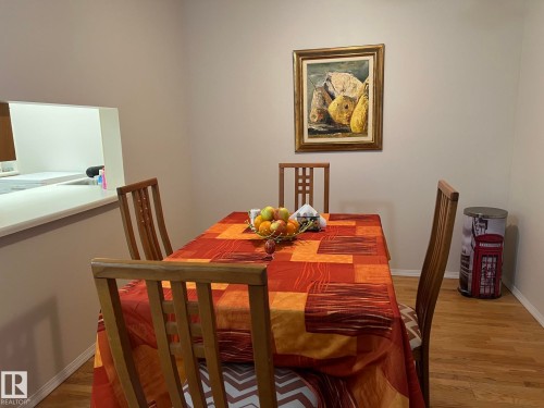 Dining area featuring wood-finish flooring and a pass-through window with white countertop - 207 18012 95 Avenue, Edmonton, AB - Indoor Photo Showing Dining Room