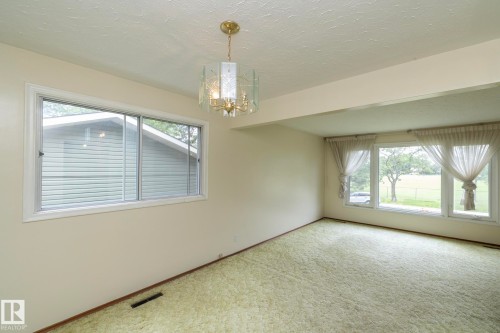 Spacious room featuring multiple windows, a decorative chandelier, and light-colored walls - 5608 122 Avenue, Edmonton, AB 