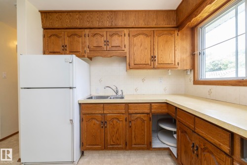 Kitchen featuring wood cabinetry, a double basin sink, a large window, a built-in refrigerator, and a corner cabinet with a lazy Susan - 5608 122 Avenue, Edmonton, AB 