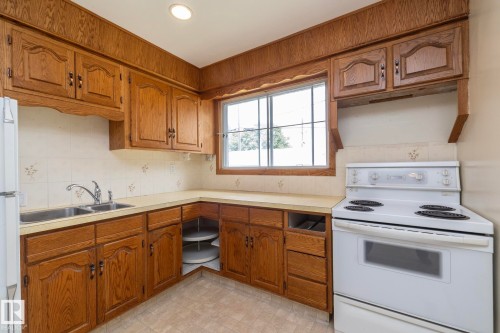 Kitchen featuring wood-finish cabinetry, a double basin stainless steel sink, a window, a white electric range, and light-toned flooring - 5608 122 Avenue, Edmonton, AB 