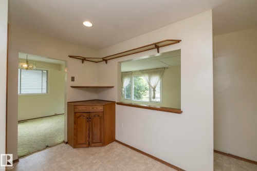 Kitchen area featuring a corner built-in cabinet with wood-finish doors, corner display shelving, and a pass-through window with a wood-finish ledge - 5608 122 Avenue, Edmonton, AB 