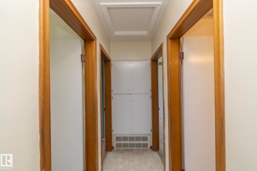 Hallway featuring light-toned wall paint, wood-finish door frames, and a visible attic access panel - 5608 122 Avenue, Edmonton, AB 