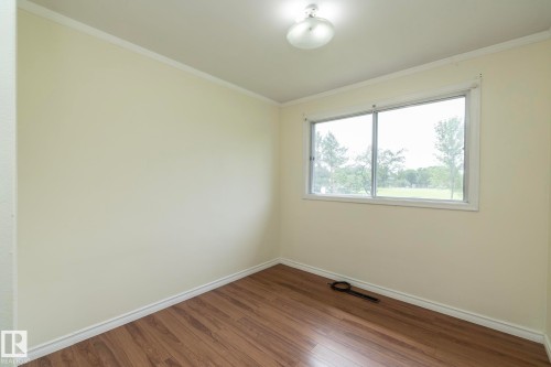 Room featuring a large window, light-colored walls, wood-finish flooring, white trim, and an overhead flush-mount light fixture - 5608 122 Avenue, Edmonton, AB 