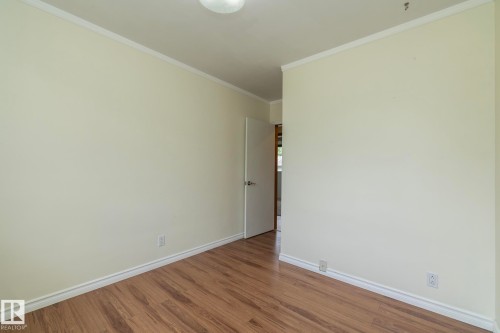 Room featuring wood-finish flooring, light-toned walls, white baseboards, and crown molding - 5608 122 Avenue, Edmonton, AB 