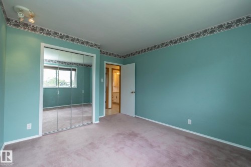 Spacious room featuring mirrored closet doors, wall-to-wall carpeting, and a visible doorway leading to an additional space - 5608 122 Avenue, Edmonton, AB 