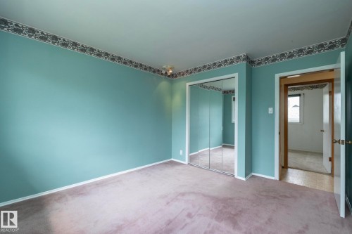 Carpeted room featuring mirrored closet doors, a patterned wallpaper border, light blue wall paint, and white baseboards - 5608 122 Avenue, Edmonton, AB 