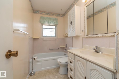 Bathroom featuring a white vanity with louvered doors and drawers, a single basin sink, and a chrome faucet - 5608 122 Avenue, Edmonton, AB 
