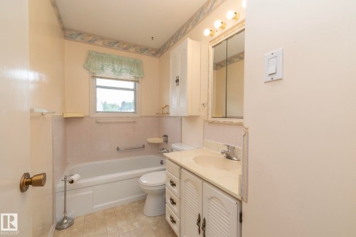 Bathroom featuring a built-in bathtub with subway tile surround, single vanity with integrated sink, chrome faucet, and a wall-mounted medicine cabinet with integrated lighting - 5608 122 Avenue, Edmonton, AB 