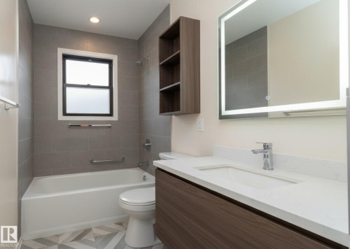 Contemporary bathroom featuring a wood-finish vanity with a white countertop and an integrated sink, illuminated by a backlit mirror - 5608 122 Avenue, Edmonton, AB 