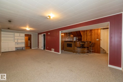 Expansive carpeted room featuring a built-in shelving unit, a paneled accent wall, and recessed lighting - 5608 122 Avenue, Edmonton, AB 