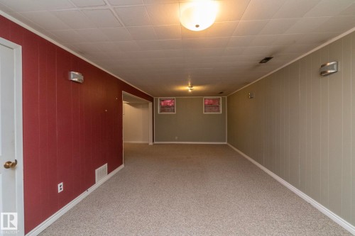 Spacious room featuring carpeting, two-tone paneling, and a drop ceiling with flush-mount lighting - 5608 122 Avenue, Edmonton, AB 