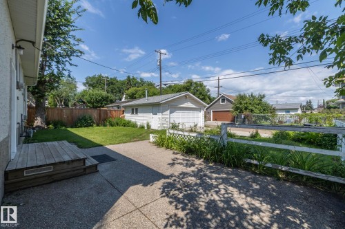 Rear yard featuring a concrete patio, wooden deck, and detached garage with a white garage door - 5608 122 Avenue, Edmonton, AB 