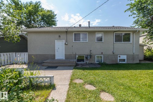 Rear exterior featuring a stucco finish, multiple windows, a concrete patio, and a grass lawn - 5608 122 Avenue, Edmonton, AB 