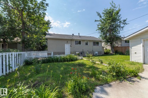 Expansive green space featuring a concrete patio, white picket fencing, mature trees, and a detached garage - 5608 122 Avenue, Edmonton, AB 