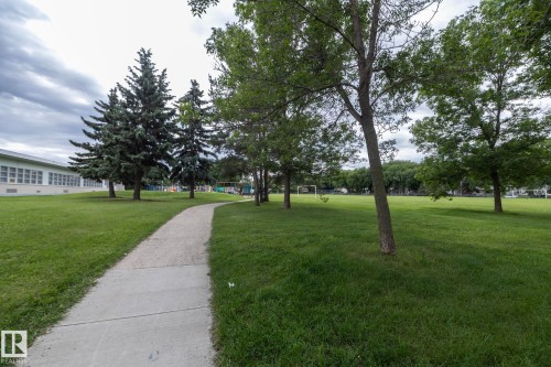 Expansive green space featuring a concrete pathway, mature trees, and a distant building with multiple windows - 5608 122 Avenue, Edmonton, AB 