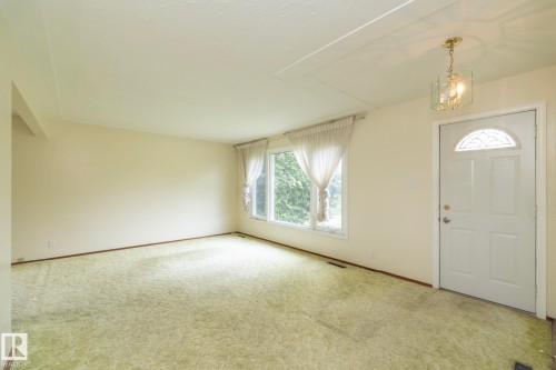 Entry foyer featuring a white door with an arched decorative glass insert, a brass-finished chandelier with clear glass panels, a picture window, and wall-to-wall carpeting - 5608 122 Avenue, Edmonton, AB 
