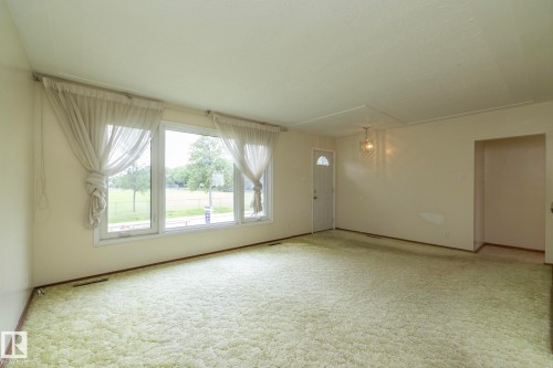 Spacious room featuring multiple windows, light-toned walls, and a front entry door with an arched glass insert - 5608 122 Avenue, Edmonton, AB 